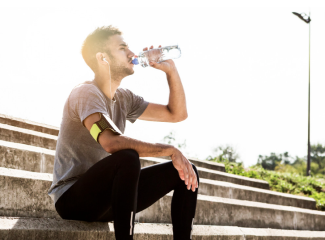 How to treat running injuries: man sitting on stairs drinking water after running outside